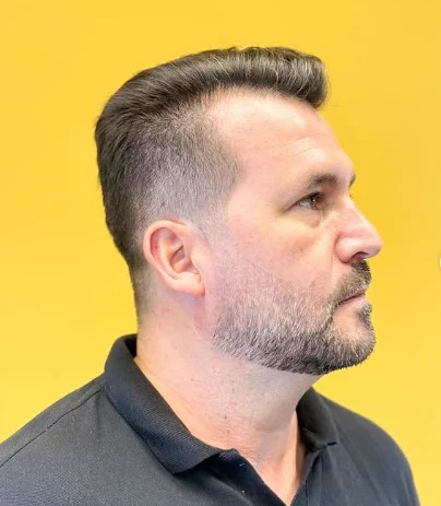 Cliente de perfil com cabelo penteado, degradê e barba na Tesoura Barbearia