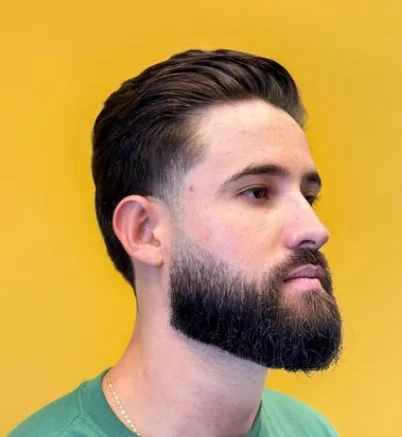 Cliente de perfil com barba cheia e cabelo repartido na Tesoura Barbearia